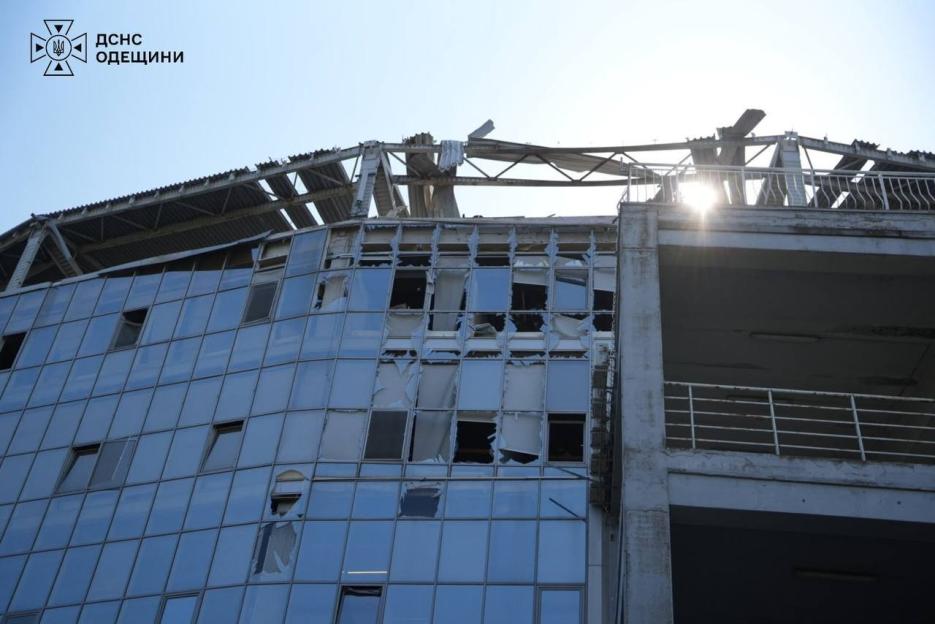 A multi-story building with a glass facade, severely damaged with shattered windows and a collapsed roof structure.