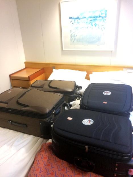 Four suitcases, two brown and two black, on a bed in a cabin.