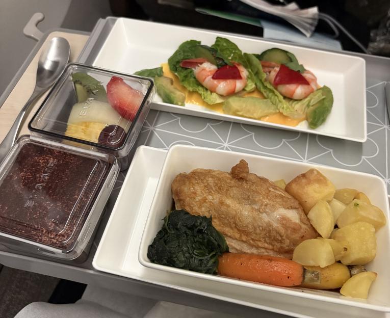 Airline meal with shrimp and avocado salad, chicken, roasted vegetables, fruit, and chocolate dessert.