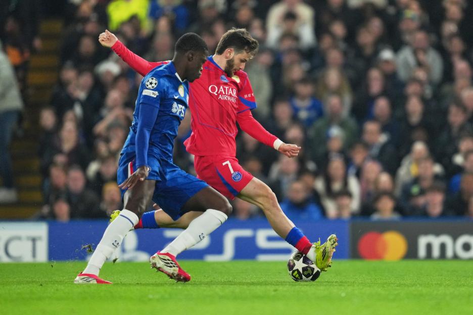 Two male soccer players, one in a blue uniform and one in a red, vie for the ball.