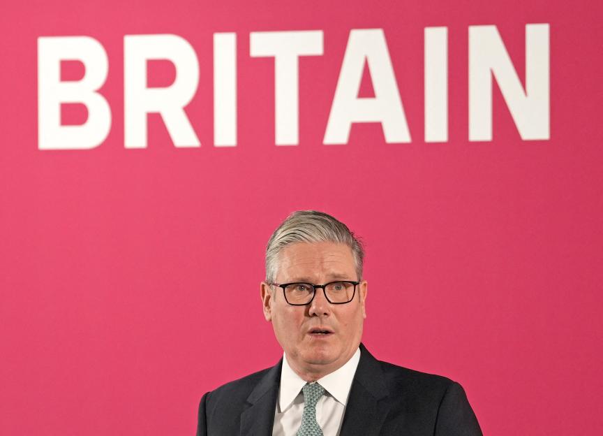 Keir Starmer speaking in London, with "BRITAIN" in white text on a pink background above him.