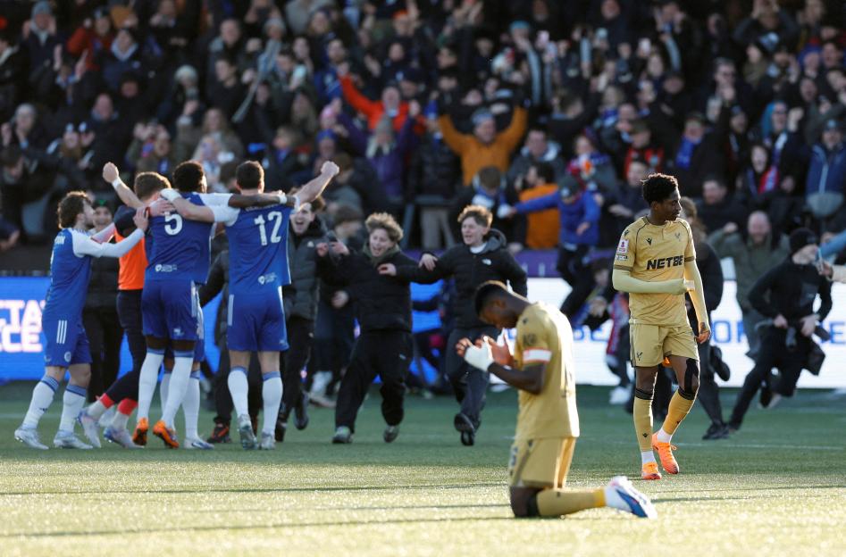Macclesfield F.C. players celebrate victory against Crystal Palace, whose player Marc Guehi kneels in dejection.