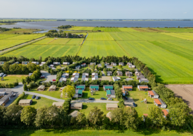 Aerial view of a campsite with bungalows and mobile homes next to green fields and a lake.