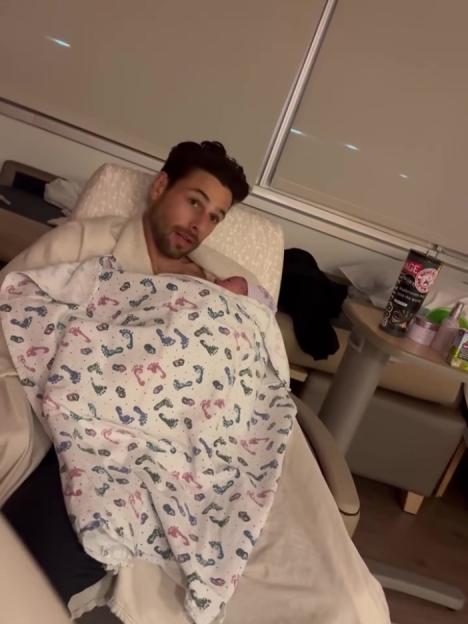 A man in a hospital gown holds a swaddled baby.