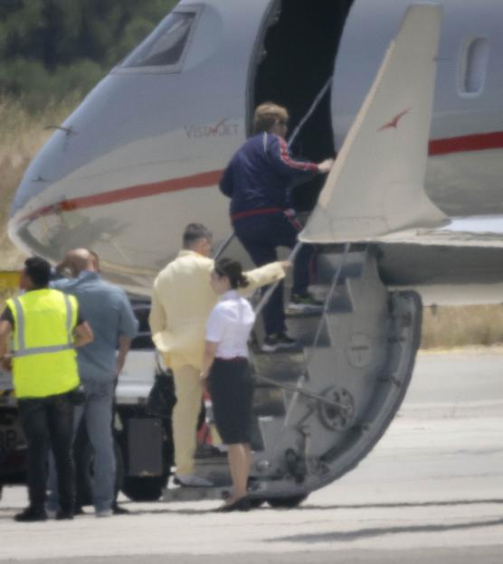 Elton John in a blue tracksuit and David Furnish in a yellow suit boarding a private jet.
