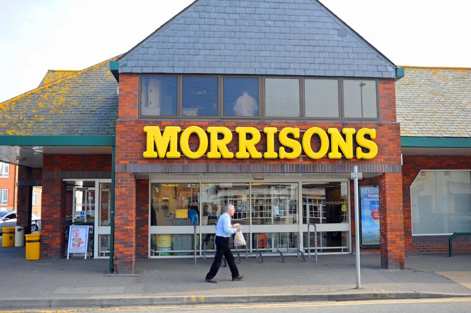 A man walking in front of a Morrisons supermarket.