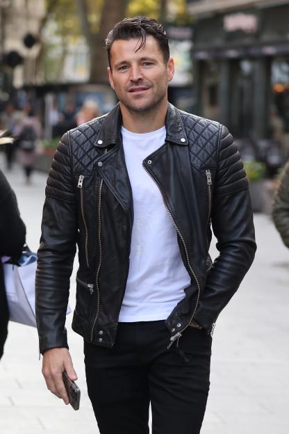 Mark Wright in a black leather biker jacket, white T-shirt, and black trousers.