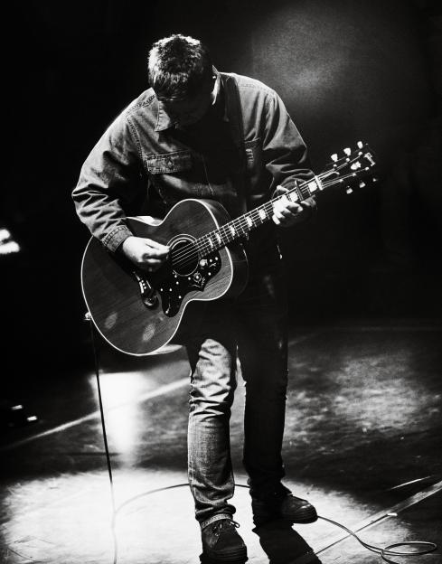 Black and white collage of Noel Gallagher playing guitar and Liam Gallagher singing at the Oasis Live '25 Tour.