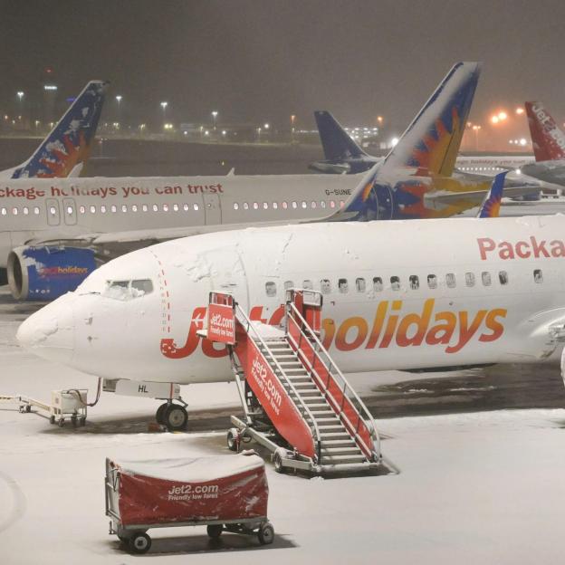 Snow-covered Jet2 airplane with boarding stairs on a runway during a snowstorm at night, with other planes visible in the background.