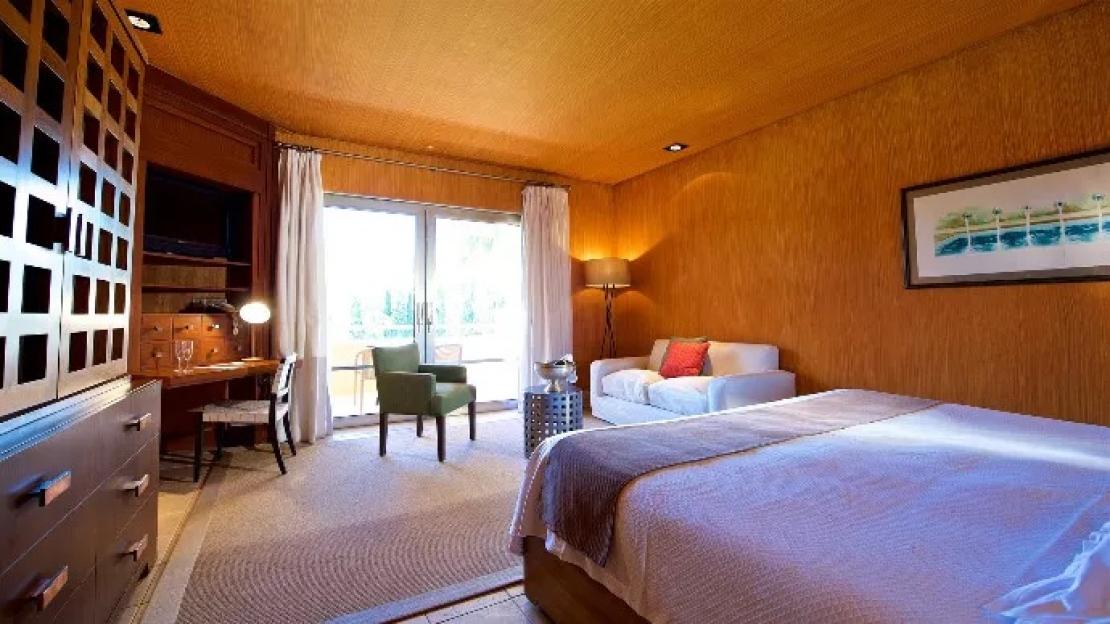Hotel room with a bed, desk, couch, and balcony.