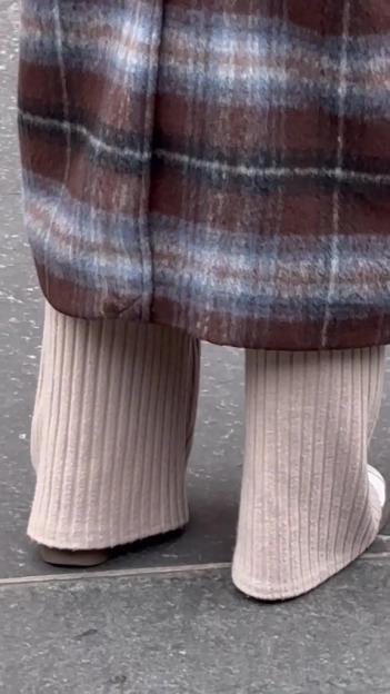 Close-up of a person wearing a brown and blue plaid coat over beige ribbed pants and flat shoes.