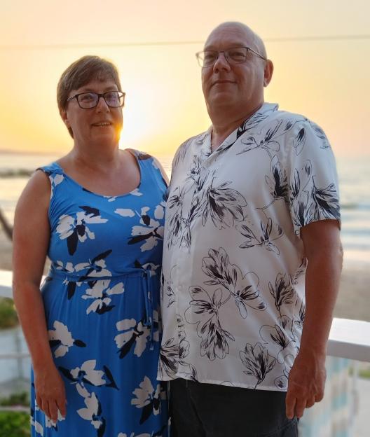 Justine Leader and a man standing outside with the ocean and sunset in the background.