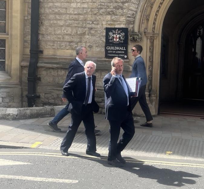 Four men walking on a street past a building with a "Guildhall City of London" sign.
