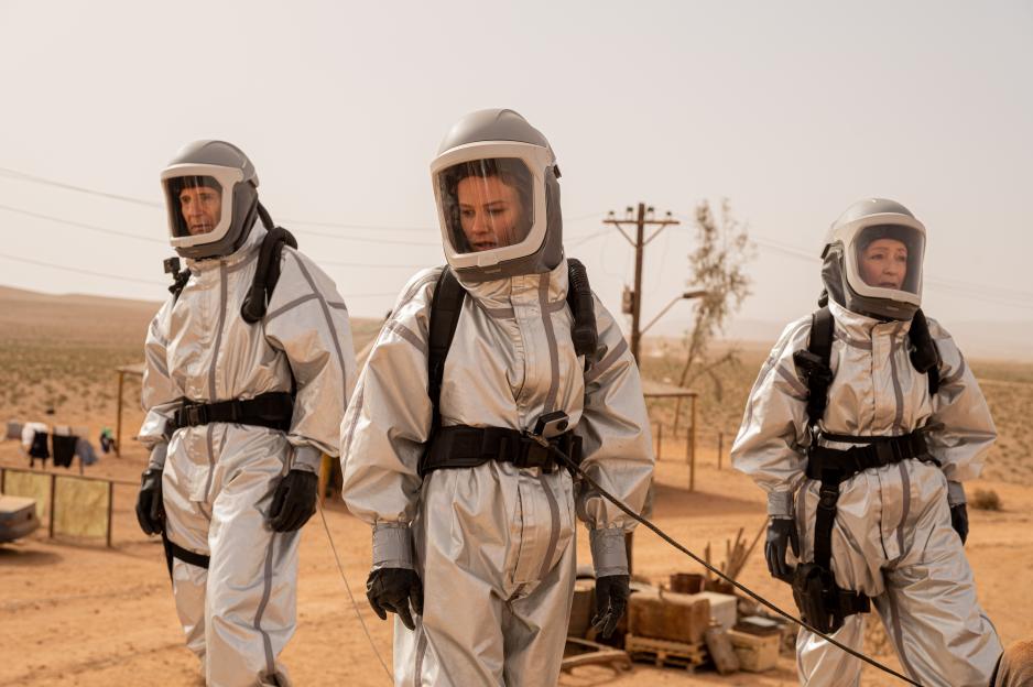 Liam Neeson, Georgina Campbell, and Lesley Manville in character as three people wearing silver hazmat suits in a desert landscape.