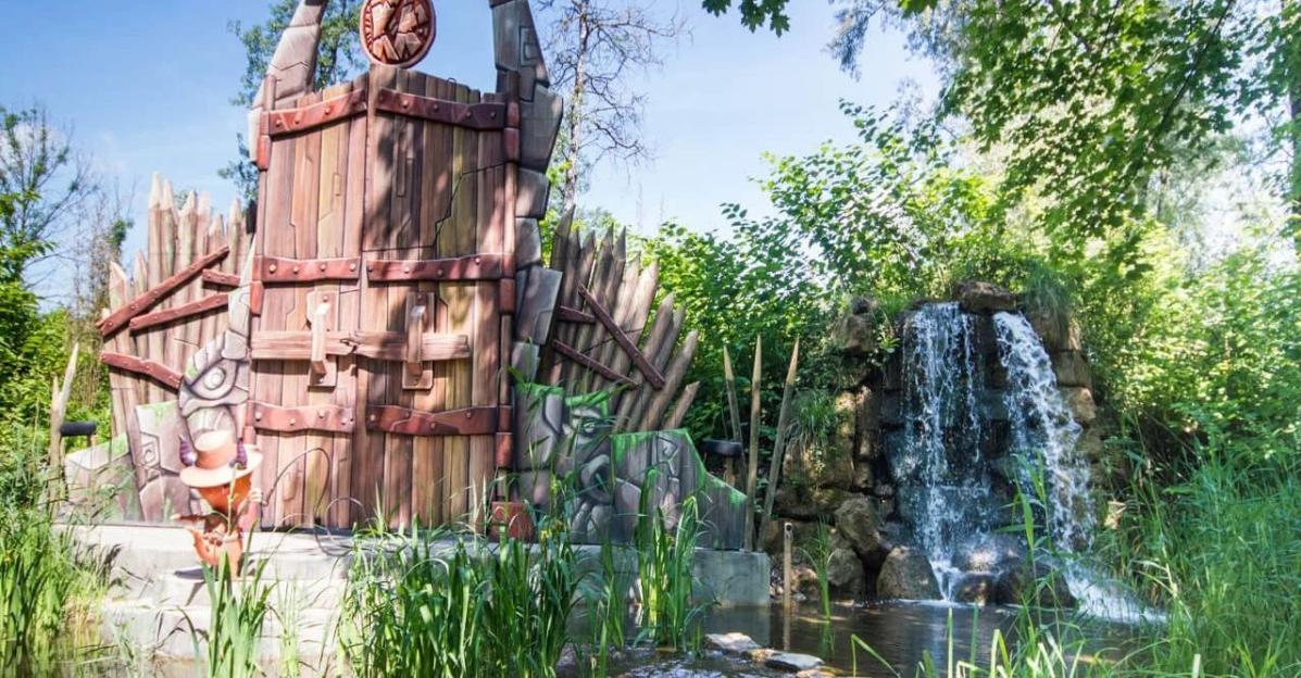 Exotic Island theme park attraction with a wooden gate, character, and waterfall.