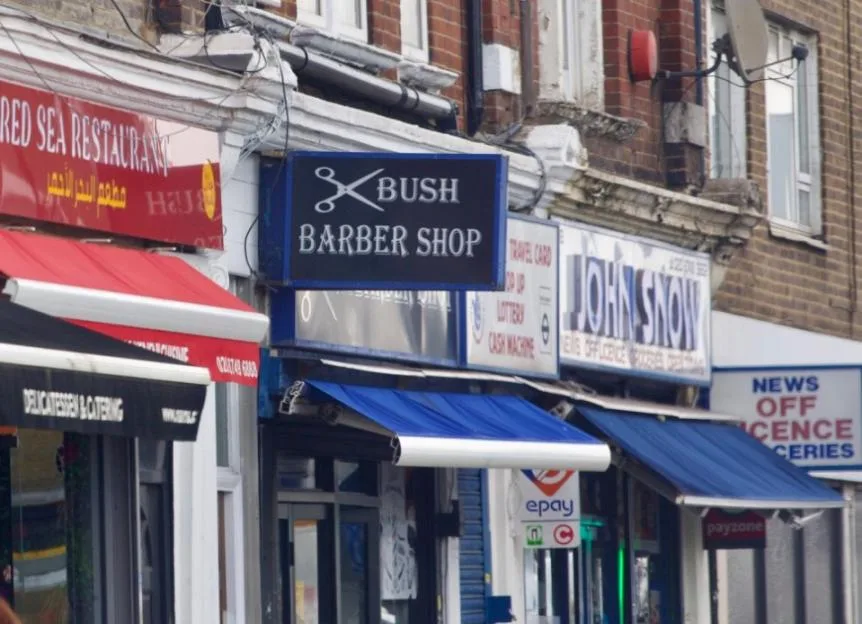 A row of shops along Uxbridge Road in London, featuring a barber shop, restaurant, and newsagent.