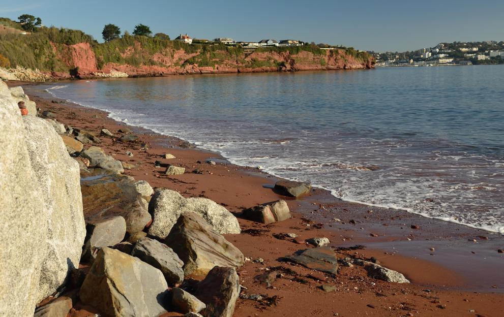 Rock armour, large boulders, piled against red sandstone cliffs on Hollicombe beach to prevent erosion.