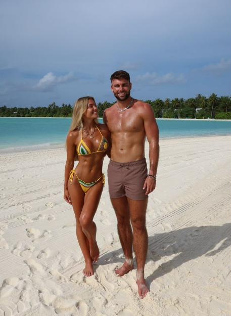 Molly Smith and Tom Clare standing sunburnt on a white sandy beach in the Maldives.