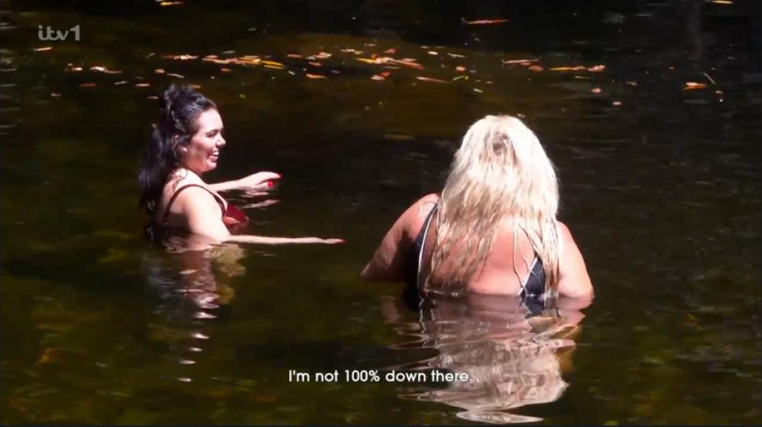 Two women in swimsuits bathing in a body of dark water.