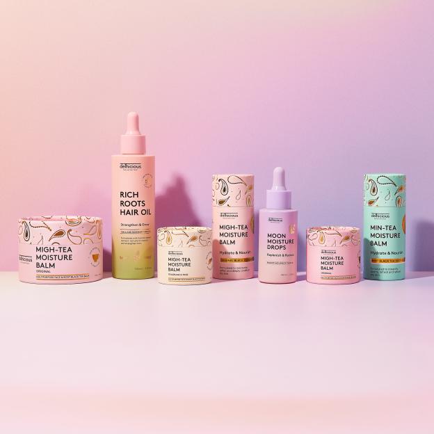A collection of Delhicious skin and hair care products including Rich Roots Hair Oil, Moon Moisture Drops, and various Migh-Tea Moisture Balms.