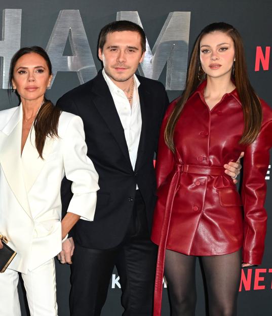 Victoria Beckham, Brooklyn Beckham, and Nicola Peltz standing together on a red carpet.