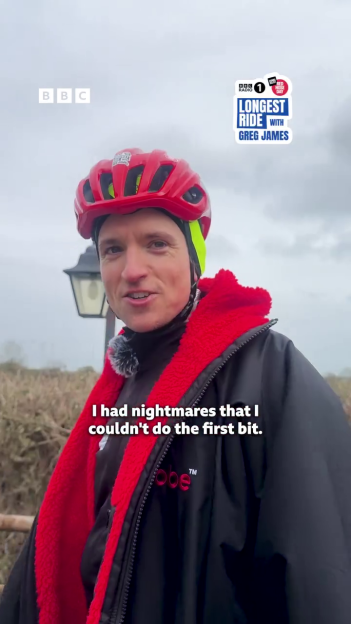 Greg James in a red helmet and black jacket talking about his Comic Relief bike ride.