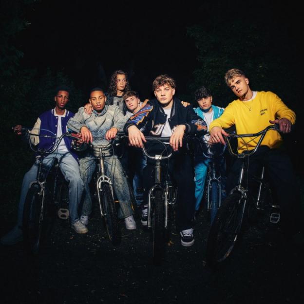 Seven young men on bicycles in a dark, outdoor setting.