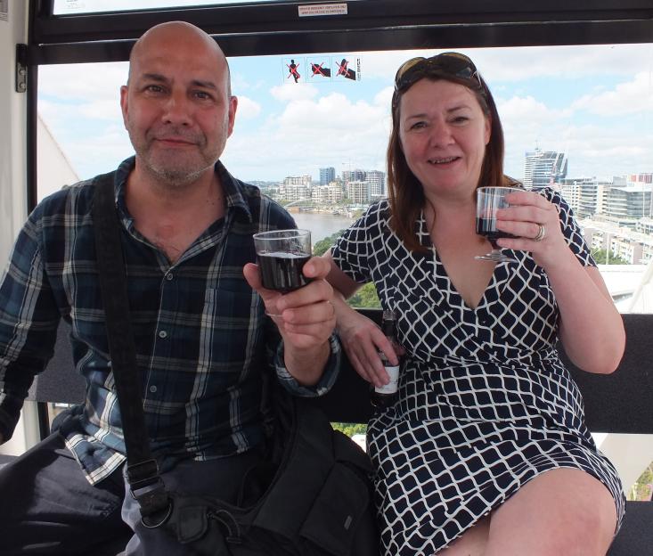 A man and a woman enjoy wine in a Ferris wheel cabin overlooking a city.