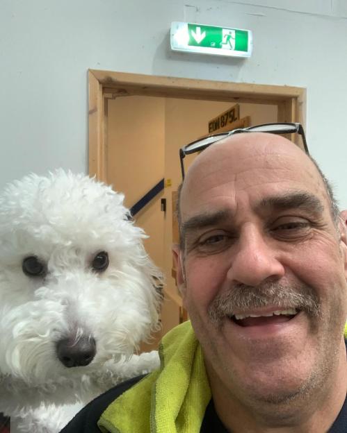 A man with a mustache and a white fluffy dog smile for a selfie.