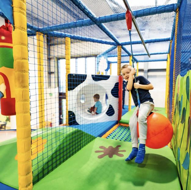Boy smiling while riding an orange ball on a zip line in an indoor playground.