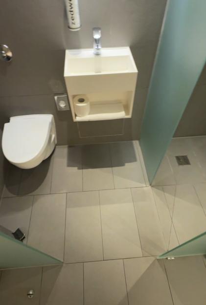 A person's feet in sandals on tiled floor in a bathroom with a toilet and sink.