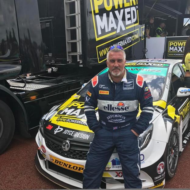 Paul Hollywood posing in a racing suit with a Power Maxed Racing BTCC car.