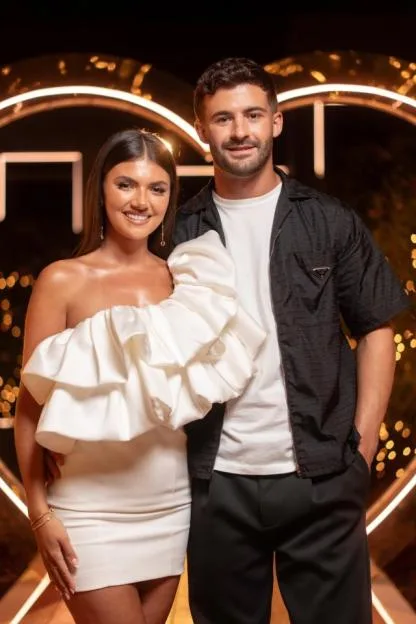 A smiling man and woman pose together in front of an illuminated heart backdrop.