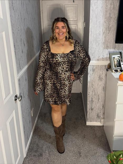 Becky Jones smiles while wearing a leopard print dress and brown boots.