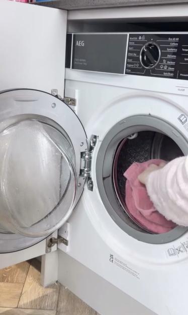 A hand placing a pink towel into an AEG 7000 Series washing machine.