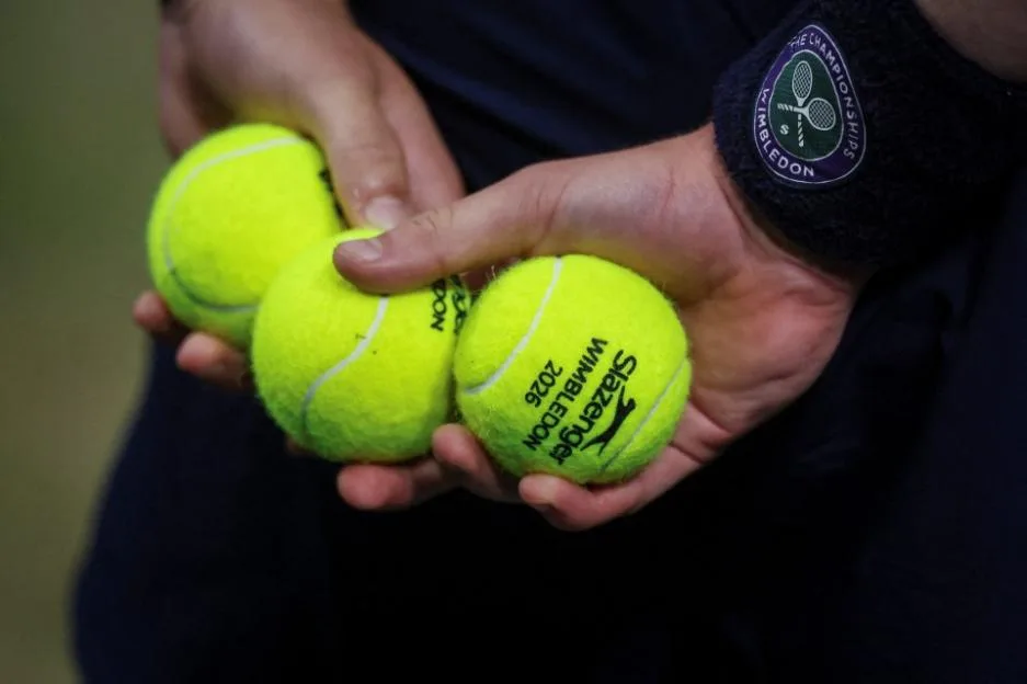 A ball kid holding three Slazenger Wimbledon 2026 tennis balls.