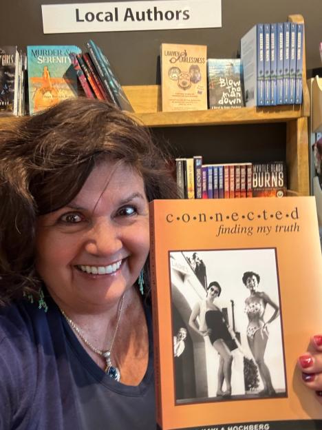 Diana Hochberg holding her book "Connected: Finding My Truth" that shares her story of being sold on the black market as a child.