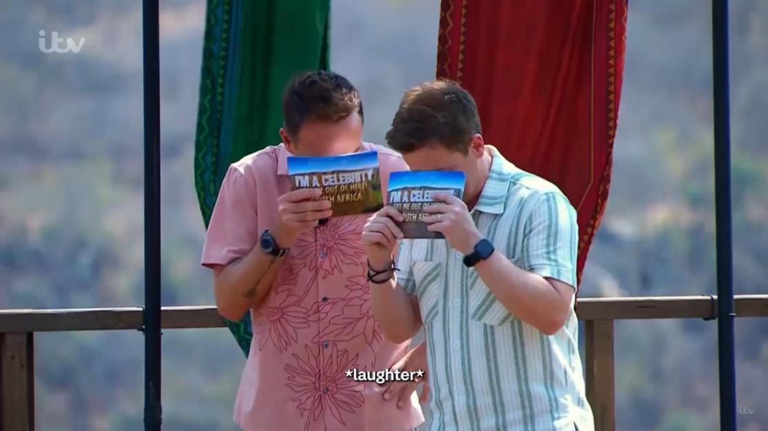 Two men holding "I'm a Celebrity... Get Me Out of Here!" cards covering their faces.