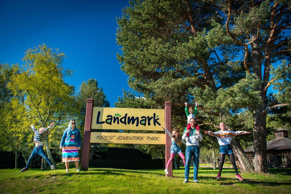 People posing in front of the Landmark Forest Adventure Park sign in Scotland.