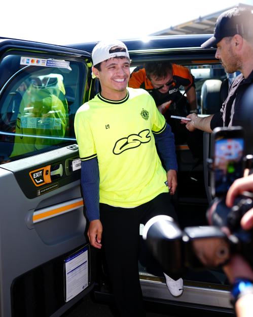 Lando Norris smiling as he steps out of a taxi at Silverstone Circuit.