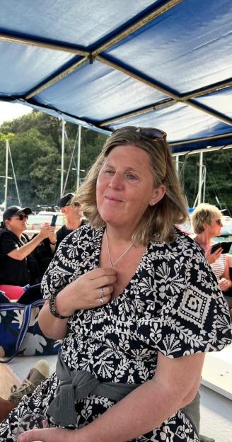 Shona Sibary, 55, sits on a boat wearing a black and white patterned dress and a silver necklace.