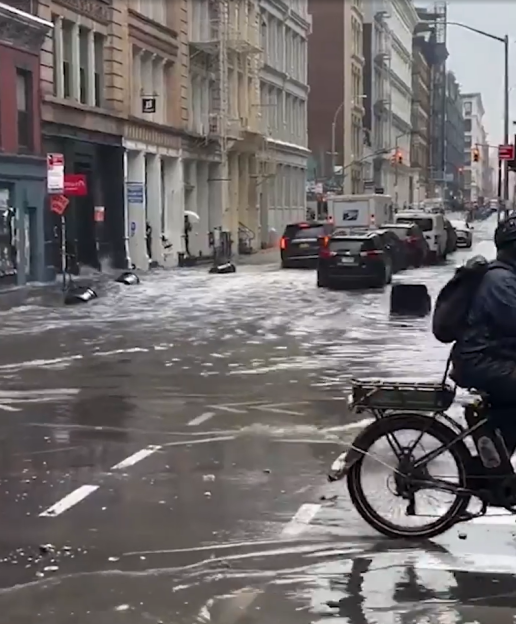 A flooded city street with cars and a person on a bicycle navigating the high water.