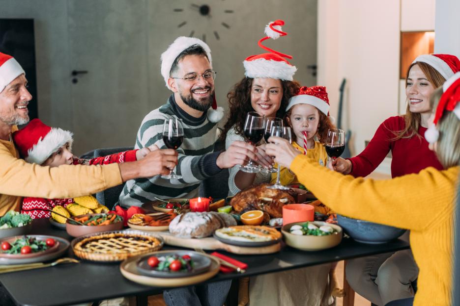 Multi-generational family in Santa hats making a toast at a Christmas dinner table filled with food.