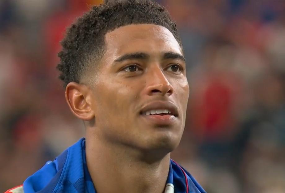 Close-up of a man with short, dark, curly hair wearing a blue and white athletic shirt, looking up and to the right.
