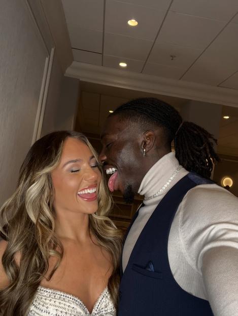 Dejon Meg laughing with a person wearing a turtleneck and suit vest.