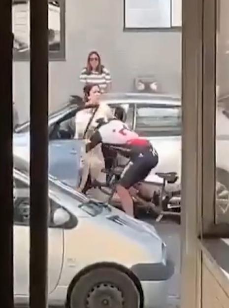 Man on a bicycle hitting the side of a car with two women looking on.
