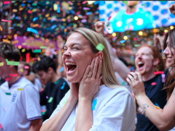 Woman cheering with hands on her face as confetti falls around her.