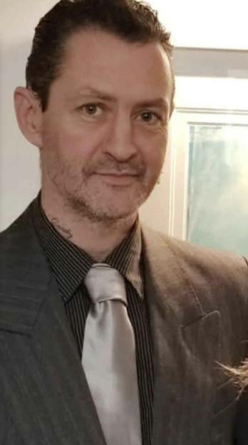 A man in a striped shirt, grey jacket, and light-colored tie.