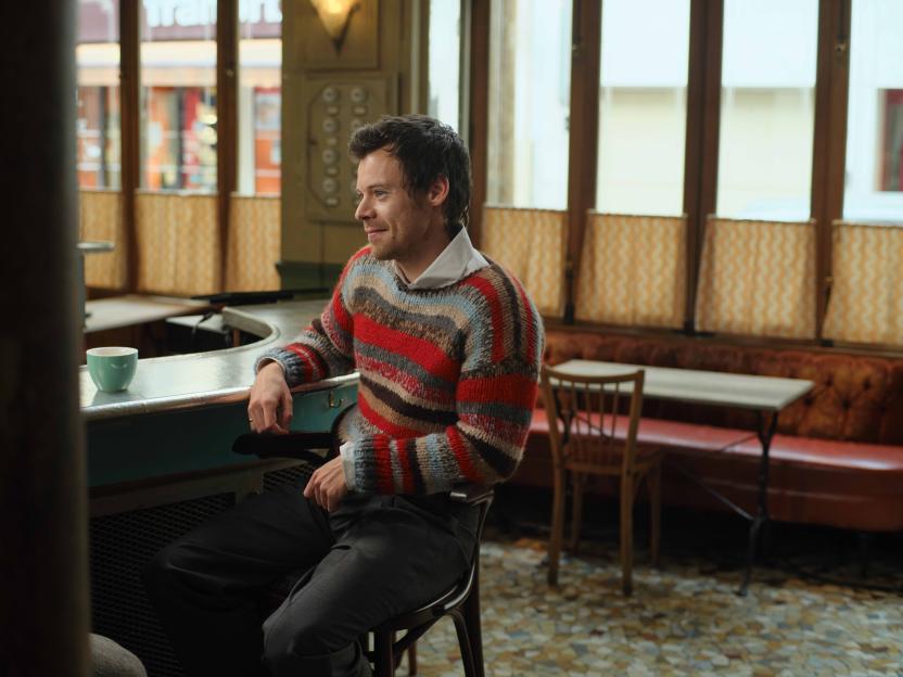 Harry Styles sitting at a bar in a striped sweater.
