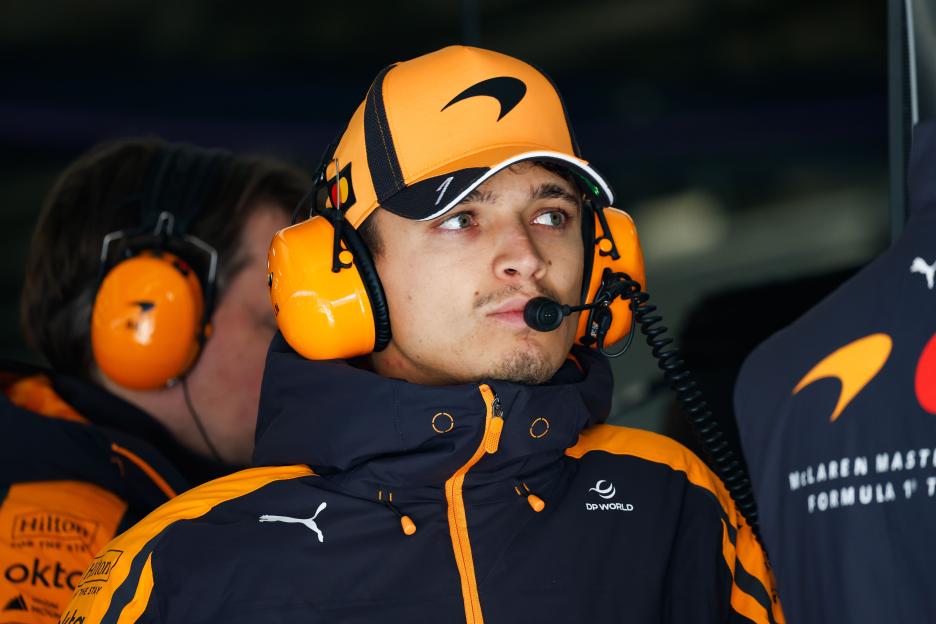 Lando Norris wearing a McLaren F1 team cap and headphones with a microphone.